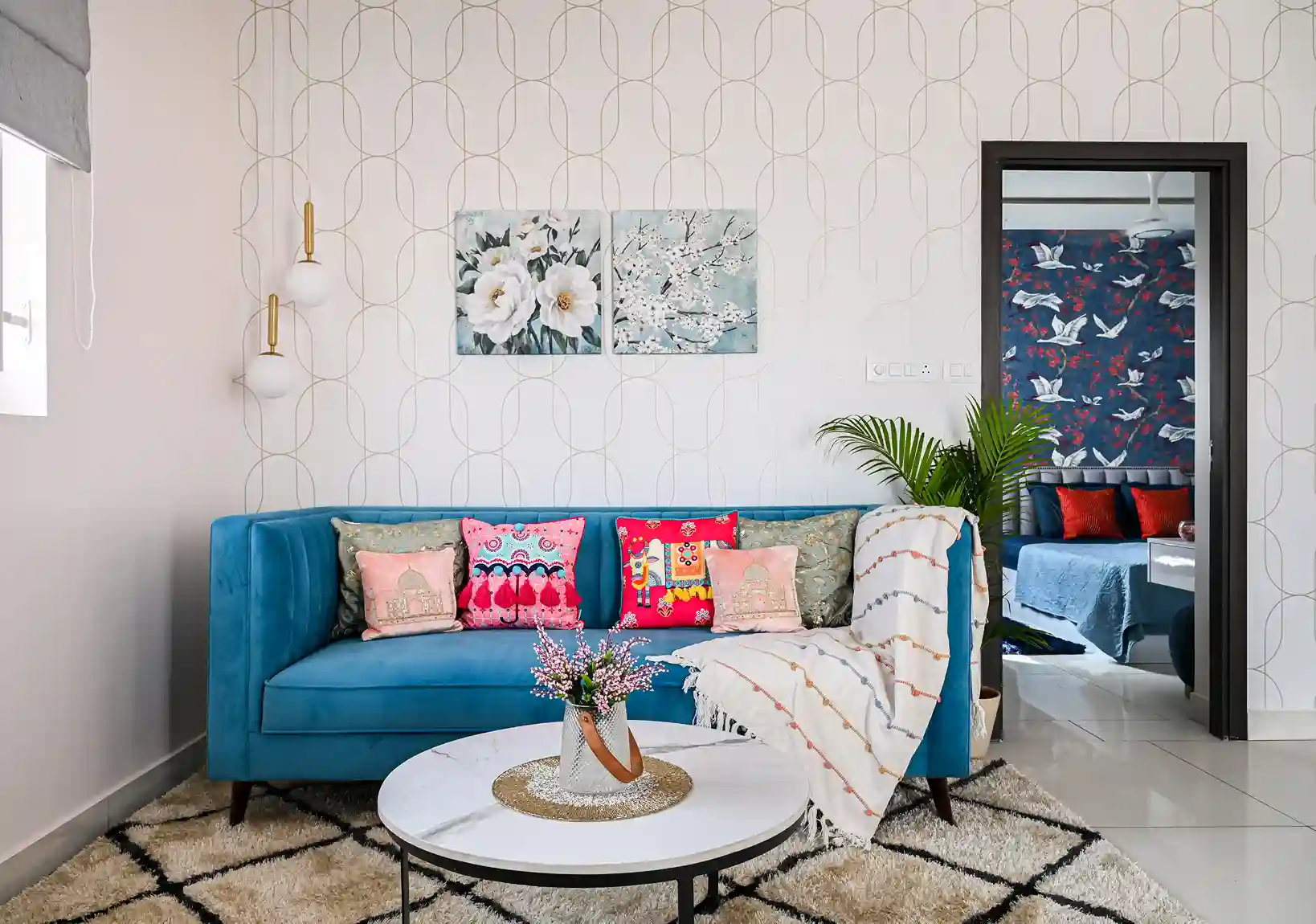 A modern living room with a blue-toned soft sofa with colorful and multi-patterned pillows. Also, a marbled coffee table